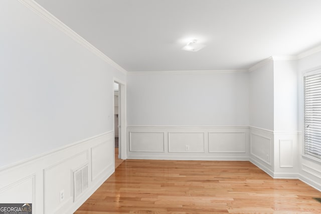 empty room with wainscoting, visible vents, light wood-style floors, and ornamental molding