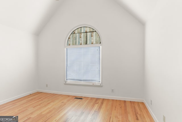 spare room featuring lofted ceiling, baseboards, wood finished floors, and visible vents