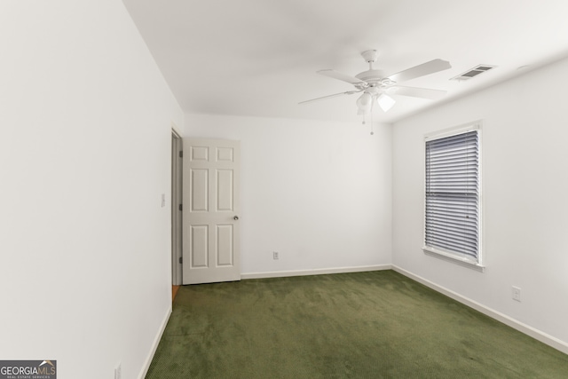 empty room featuring dark colored carpet, visible vents, a ceiling fan, and baseboards