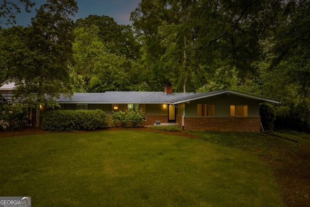 ranch-style home featuring a chimney, brick siding, and a front yard