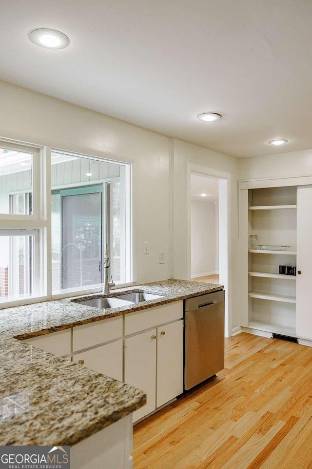 kitchen with light stone counters, dishwasher, a sink, light wood-type flooring, and white cabinetry