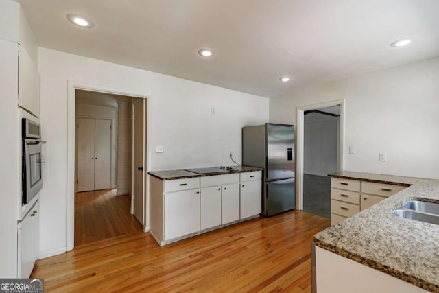kitchen featuring white cabinets, appliances with stainless steel finishes, light wood finished floors, and stone counters