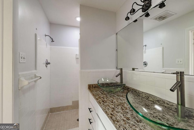 bathroom featuring wainscoting, vanity, tile walls, a tile shower, and visible vents