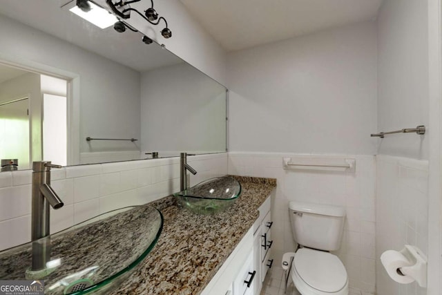 bathroom with tile walls, a wainscoted wall, vanity, and toilet