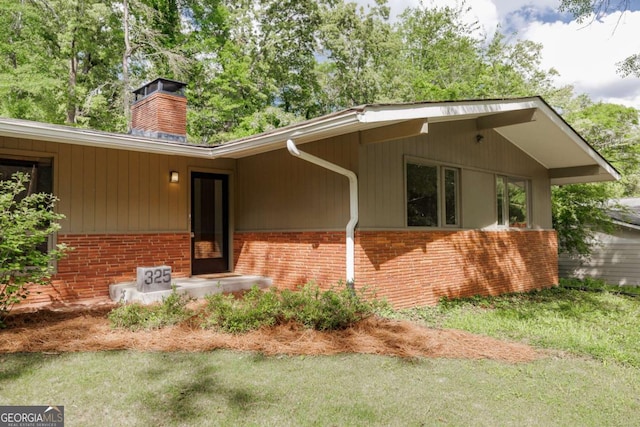 exterior space with a chimney, brick siding, and a lawn