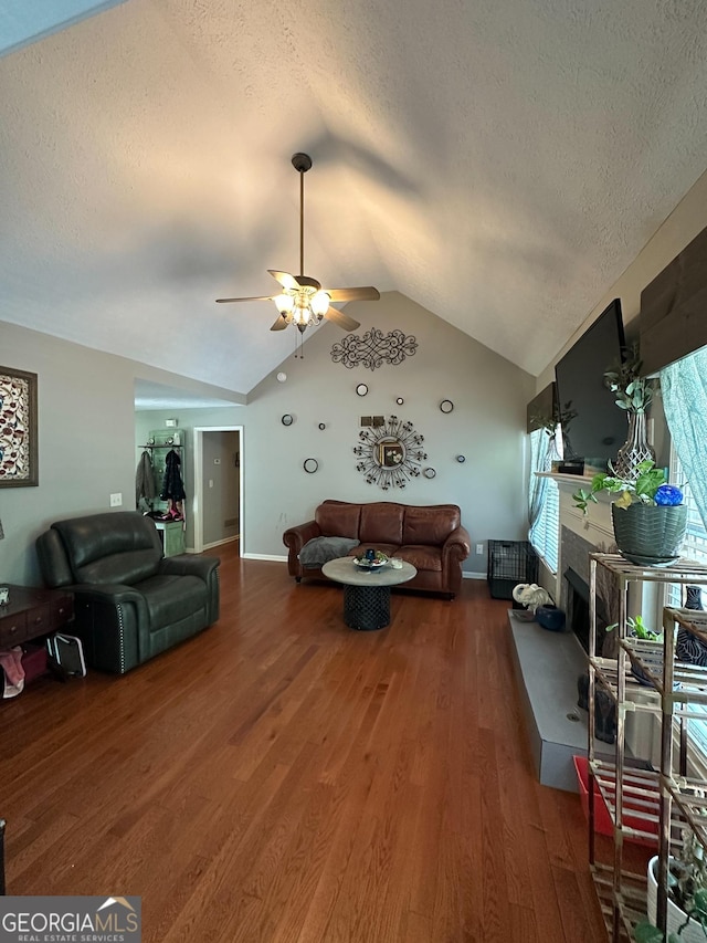 living area featuring ceiling fan, a fireplace with raised hearth, a textured ceiling, wood finished floors, and vaulted ceiling
