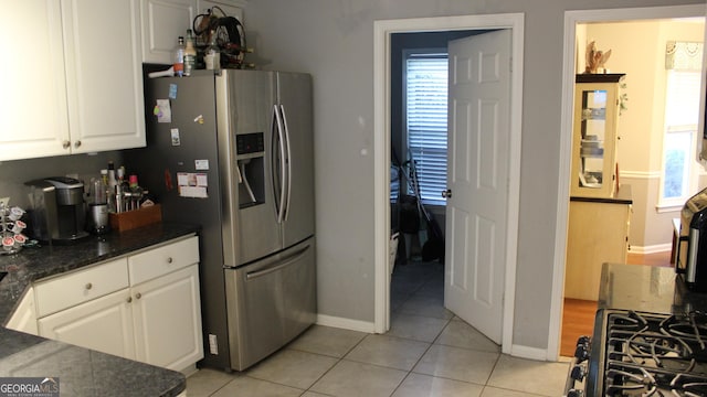 kitchen with light tile patterned flooring, dark countertops, stainless steel fridge with ice dispenser, white cabinetry, and baseboards