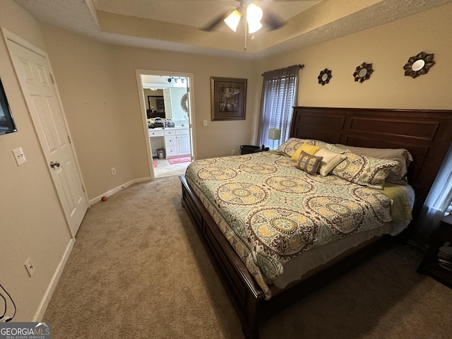 bedroom with ceiling fan, light colored carpet, baseboards, connected bathroom, and a tray ceiling