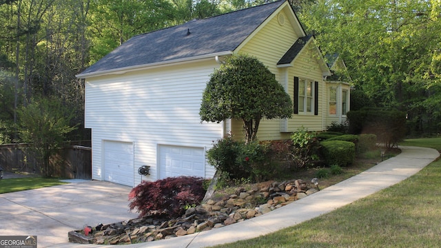 view of side of property with a garage, roof with shingles, fence, and concrete driveway