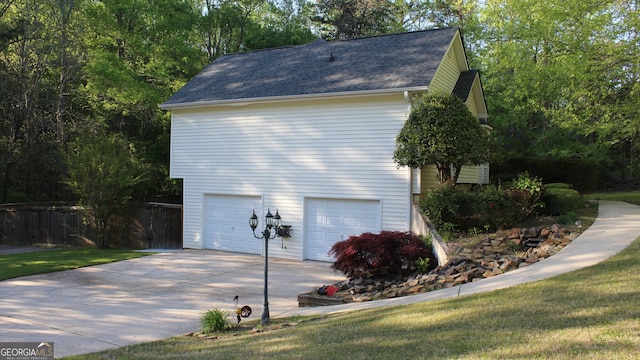 view of side of property with an attached garage, roof with shingles, fence, and concrete driveway
