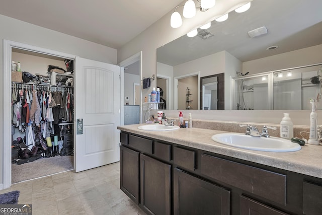 bathroom with double vanity, a spacious closet, a stall shower, and a sink