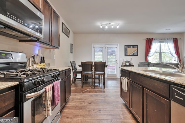 kitchen with appliances with stainless steel finishes, dark brown cabinets, light wood finished floors, and a sink