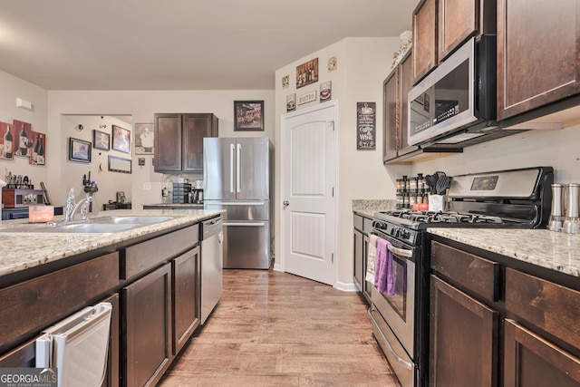 kitchen with dark brown cabinetry, light wood-style flooring, light stone counters, appliances with stainless steel finishes, and a sink