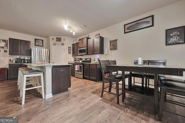 kitchen with a kitchen bar, stainless steel appliances, dark brown cabinets, and light wood-style flooring