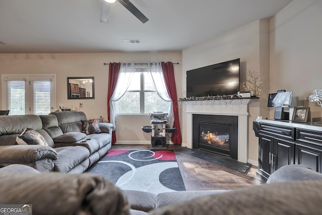 living area with wood finished floors, ceiling fan, a glass covered fireplace, baseboards, and visible vents