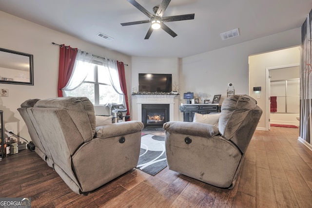 living area featuring wood finished floors, visible vents, a glass covered fireplace, and a ceiling fan