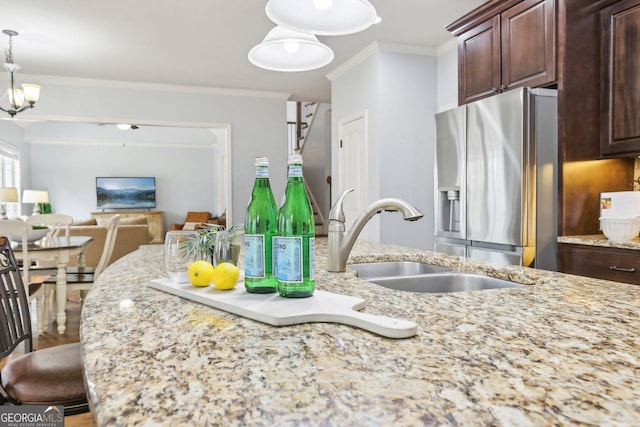 108 Turnberry Trce, Sharpsburg, GA 30277 - kitchen with stainless steel fridge, light stone counters, dark brown cabinets, ornamental molding, and decorative light fixtures