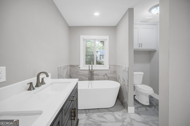 bathroom with a sink, toilet, marble finish floor, a freestanding bath, and double vanity