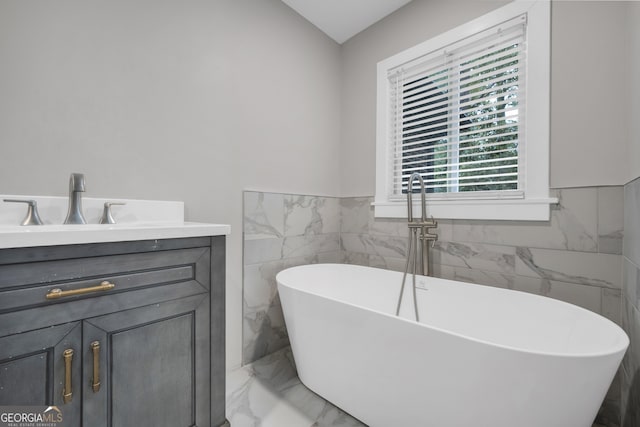 full bath with marble finish floor, tile walls, a freestanding tub, a wainscoted wall, and vanity