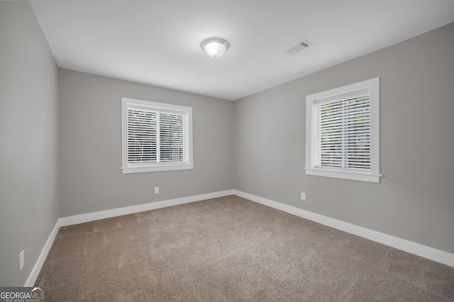 carpeted spare room featuring a healthy amount of sunlight, visible vents, and baseboards