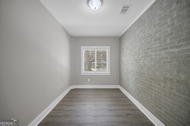 unfurnished room with baseboards, visible vents, dark wood finished floors, and brick wall