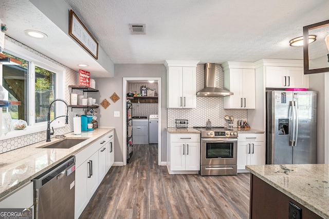 205 Tamea Trl, Covington, GA 30014 - kitchen featuring wall chimney range hood, appliances with stainless steel finishes, a sink, washer and clothes dryer, and white cabinetry