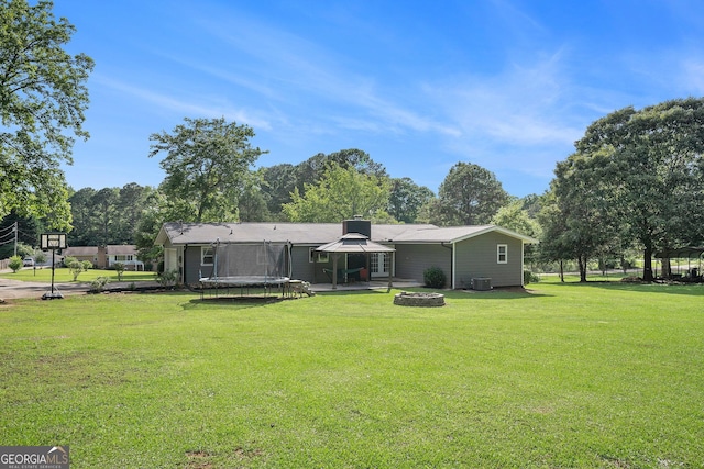 205 Tamea Trl, Covington, GA 30014 - rear view of property featuring a trampoline, an outdoor fire pit, a lawn, a patio area, and central AC unit
