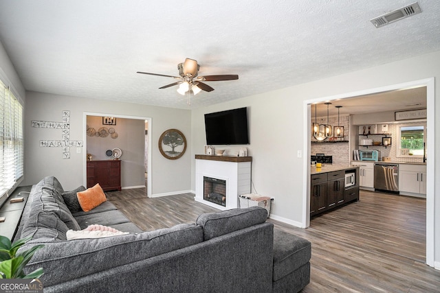 205 Tamea Trl, Covington, GA 30014 - living area with dark wood finished floors, a glass covered fireplace, ceiling fan, baseboards, and a textured ceiling