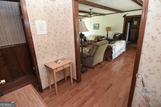 living area featuring beam ceiling, wood finished floors, ceiling fan, and wallpapered walls