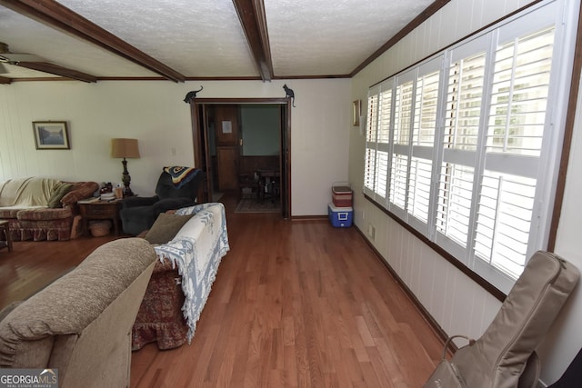 living room with crown molding, beamed ceiling, a textured ceiling, and wood finished floors