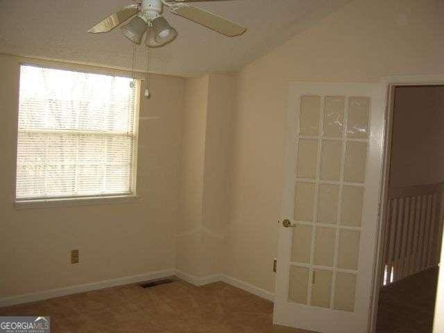 empty room with lofted ceiling, visible vents, baseboards, and ceiling fan