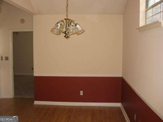 unfurnished dining area featuring vaulted ceiling, wood finished floors, baseboards, and a notable chandelier