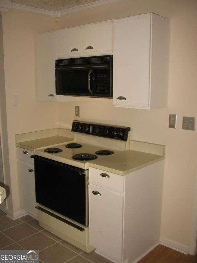 kitchen with light countertops, ornamental molding, white range with electric cooktop, black microwave, and white cabinetry