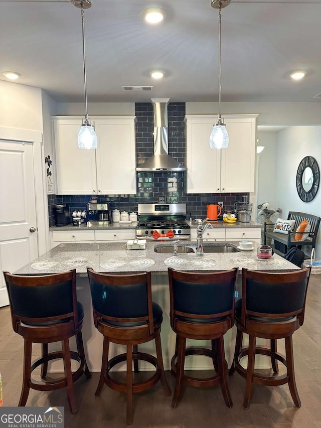 kitchen featuring visible vents, stainless steel gas range, wall chimney exhaust hood, and decorative backsplash