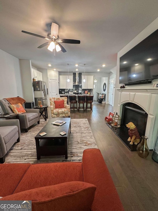 living area with wood finished floors, ceiling fan, and a fireplace with raised hearth