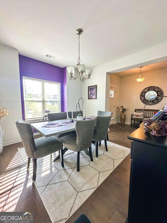 dining room featuring baseboards, visible vents, wood finished floors, and an inviting chandelier