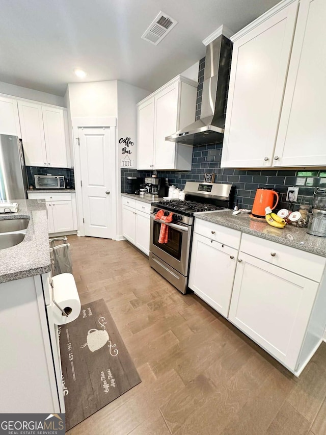 kitchen with white cabinetry, tasteful backsplash, appliances with stainless steel finishes, visible vents, and wall chimney exhaust hood