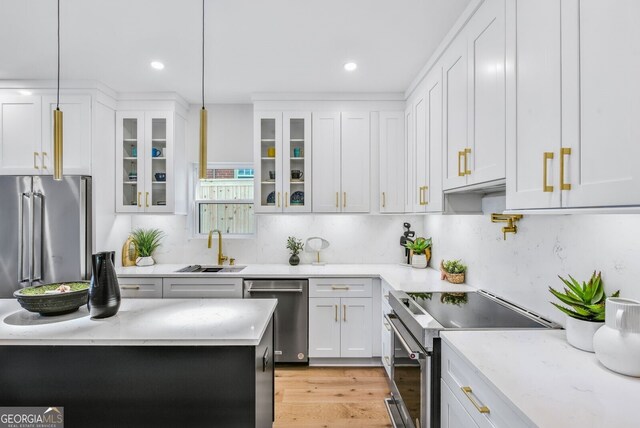kitchen with white cabinets, light stone counters, a sink, stainless steel appliances, and glass insert cabinets