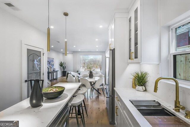 kitchen with visible vents, wood finished floors, light stone countertops, glass insert cabinets, and a sink
