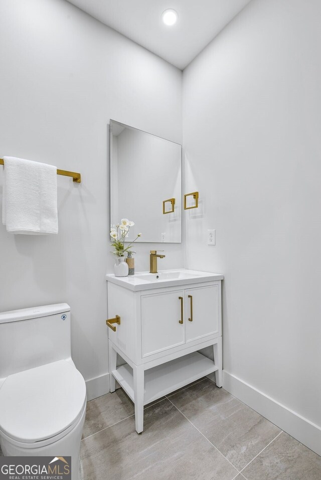 half bath featuring baseboards, tile patterned flooring, toilet, and vanity