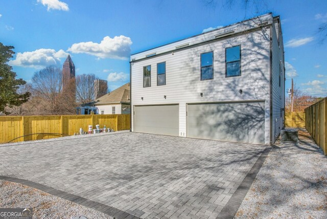 view of side of property with an attached garage, decorative driveway, fence, and cooling unit