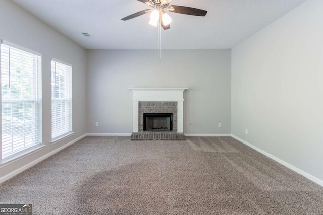 unfurnished living room with a ceiling fan, a brick fireplace, a healthy amount of sunlight, and carpet