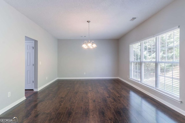 empty room with a textured ceiling, baseboards, dark wood-style flooring, an inviting chandelier, and visible vents