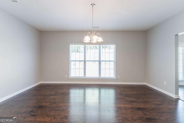 empty room with a chandelier, dark wood-style flooring, and baseboards