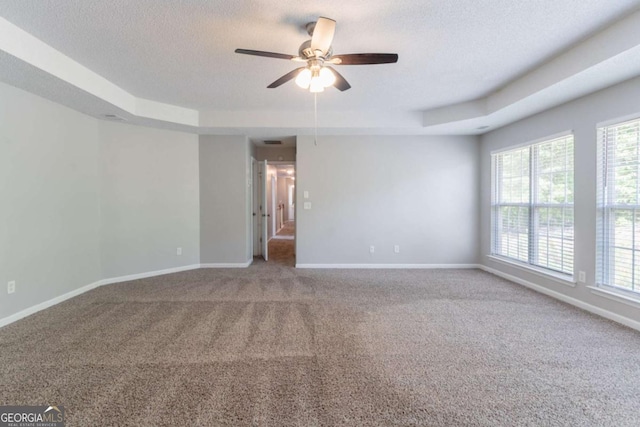 carpeted empty room with a tray ceiling, baseboards, a ceiling fan, and a healthy amount of sunlight