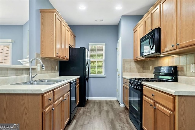 kitchen with decorative backsplash, light countertops, a sink, light wood-style flooring, and black appliances