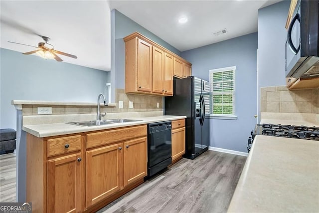 kitchen with a sink, light wood-style floors, a ceiling fan, backsplash, and black appliances