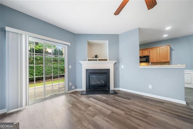 unfurnished living room featuring a glass covered fireplace, baseboards, dark wood-type flooring, recessed lighting, and a ceiling fan