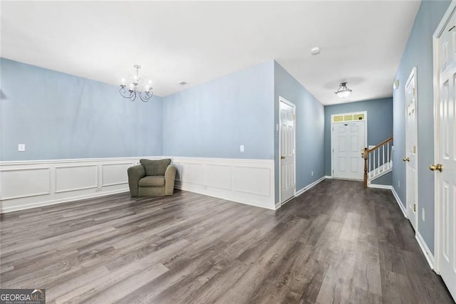 unfurnished room with a decorative wall, a chandelier, a wainscoted wall, wood finished floors, and stairway