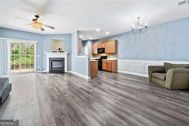 living room with visible vents, a glass covered fireplace, recessed lighting, dark wood-type flooring, and ceiling fan with notable chandelier